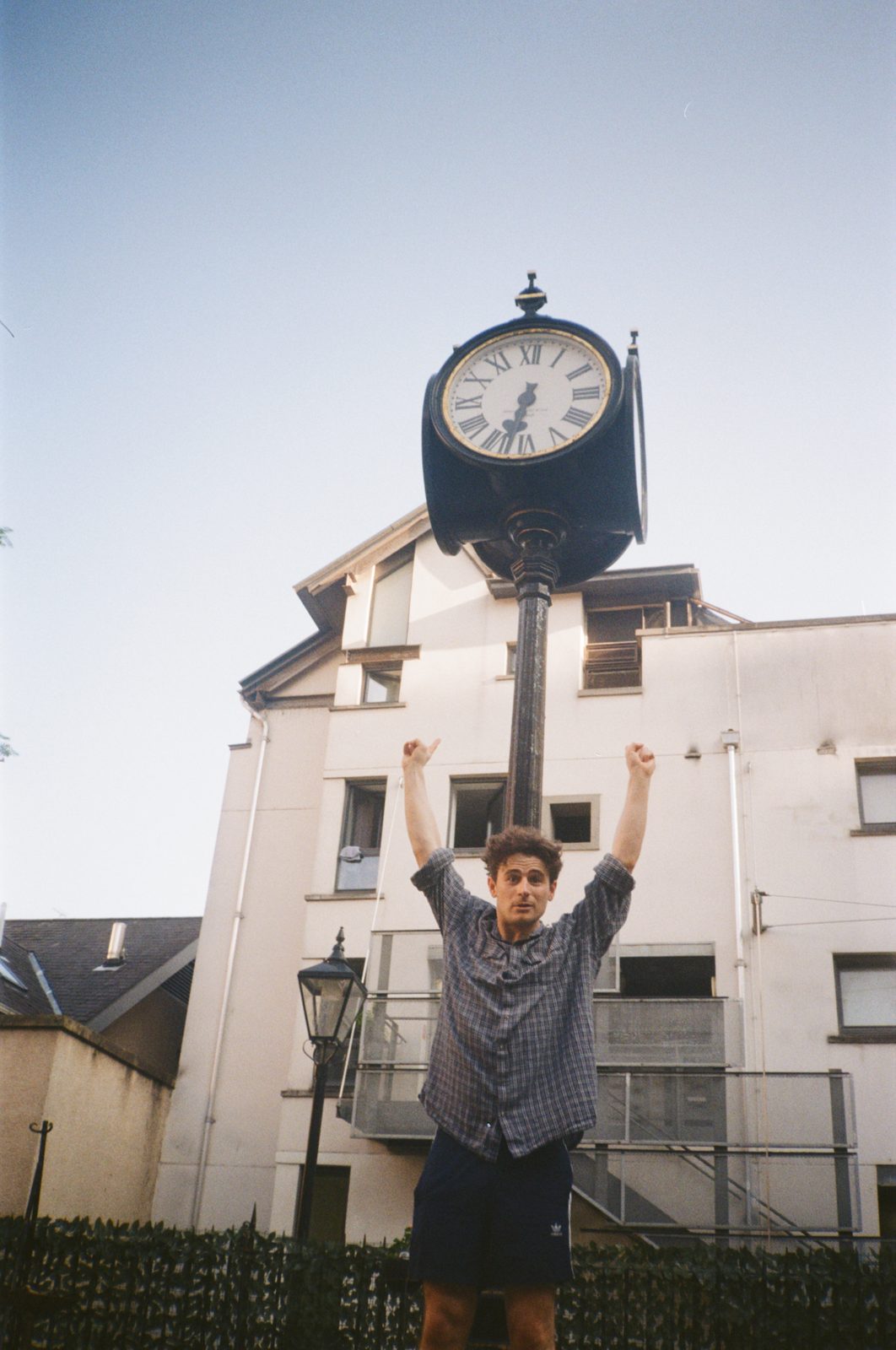 alex with his arms up under a large street clock
