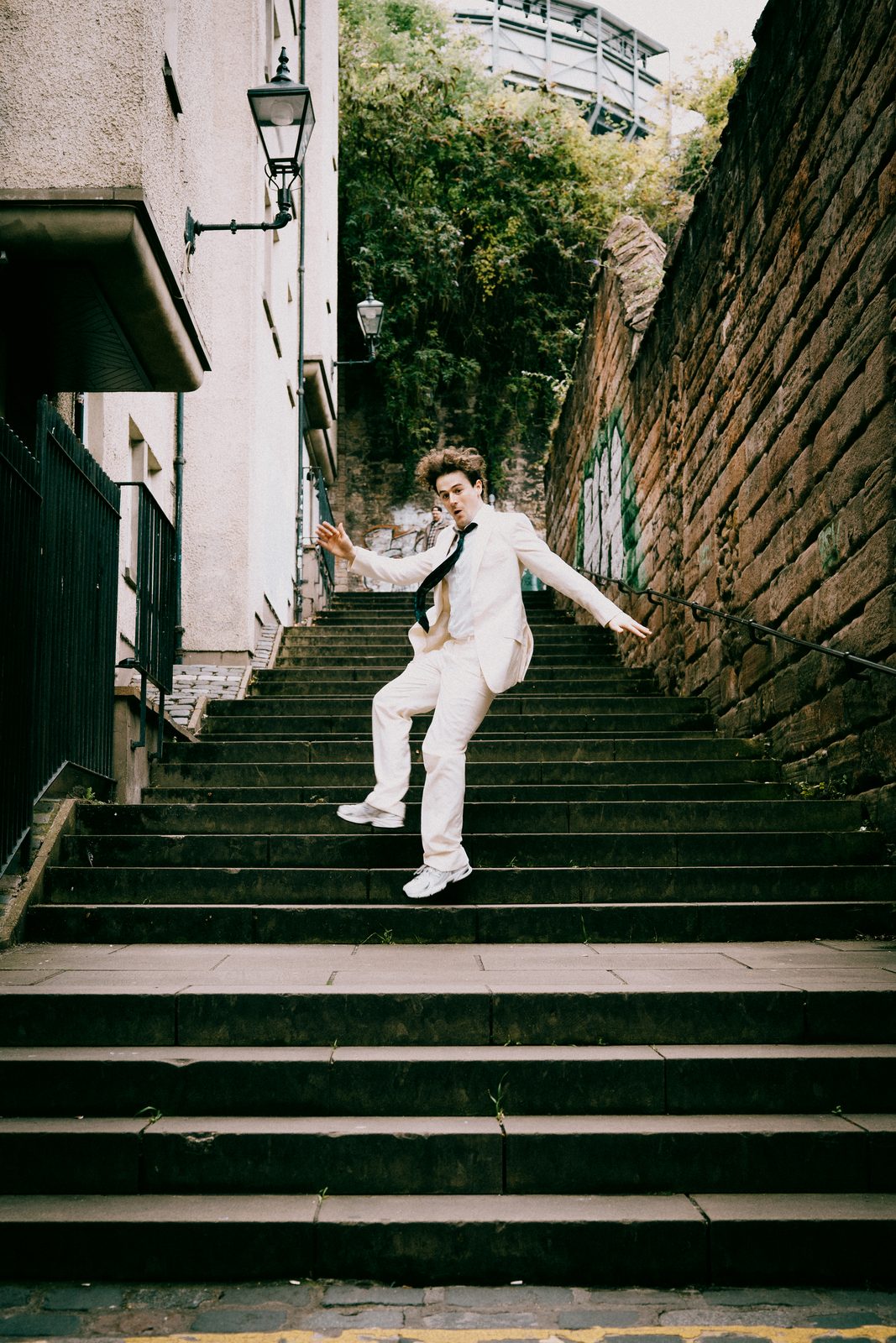 alex in a white suit mid-leap down a flight of stone steps